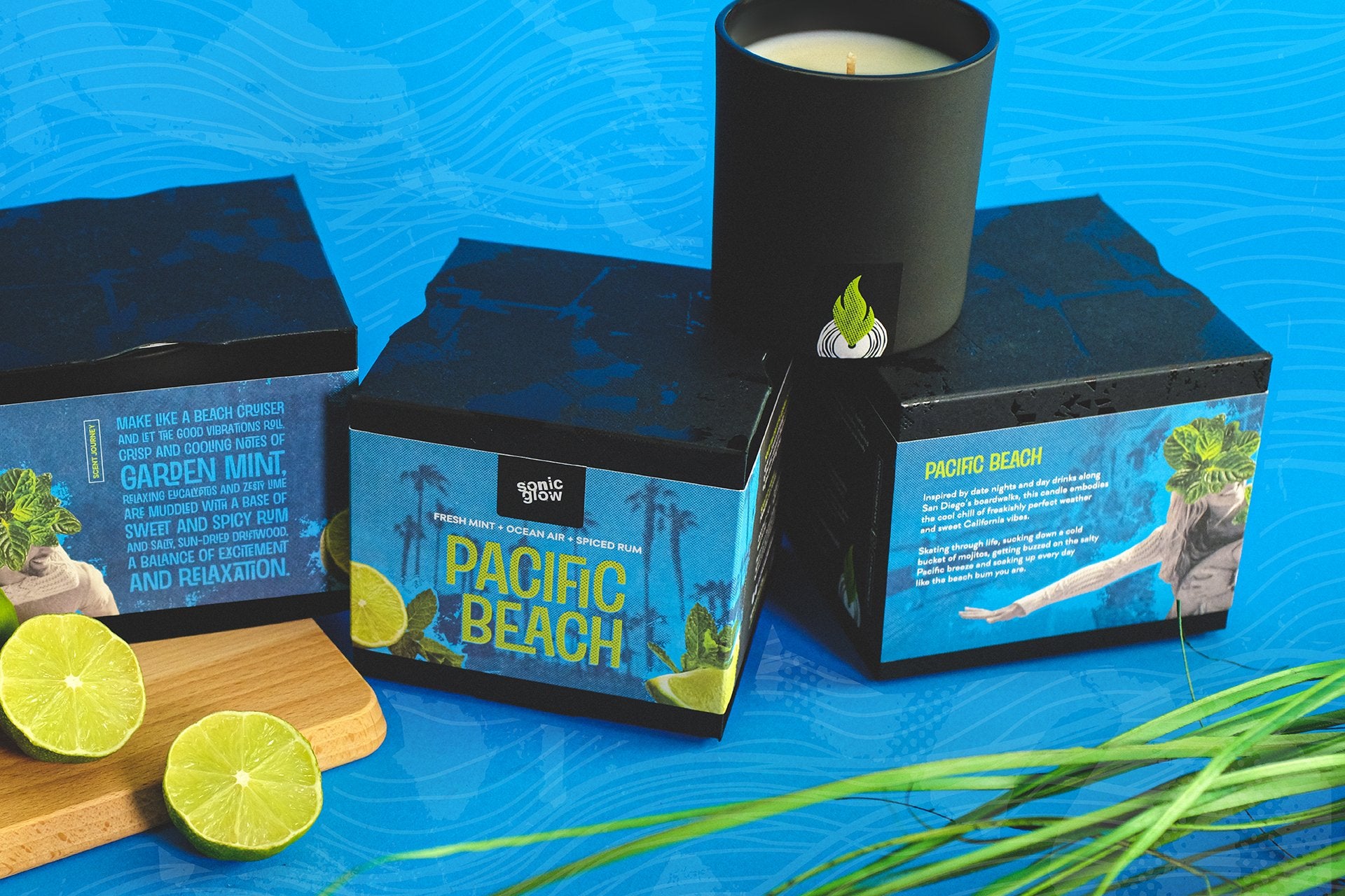 Sonicglow Pacific Beach candle and packaging, styled with fresh cut limes and beach grasses, on a textured blue background 